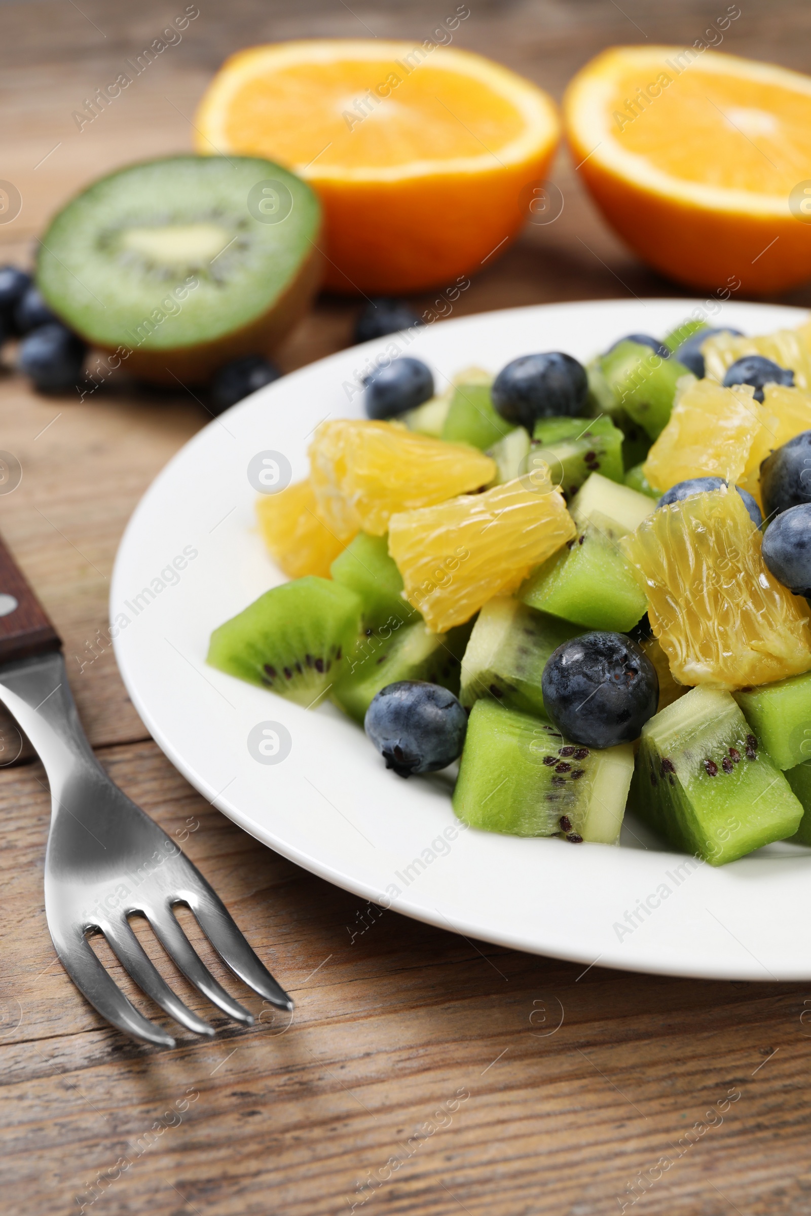 Photo of Plate of tasty fruit salad and fork on wooden table, closeup