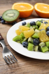 Plate of tasty fruit salad and fork on wooden table, closeup