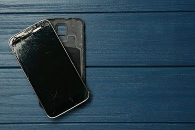 Photo of Damaged smartphone on blue wooden table, top view with space for text. Device repairing