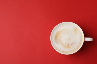 Photo of Tasty cappuccino in coffee cup on red background, top view. Space for text