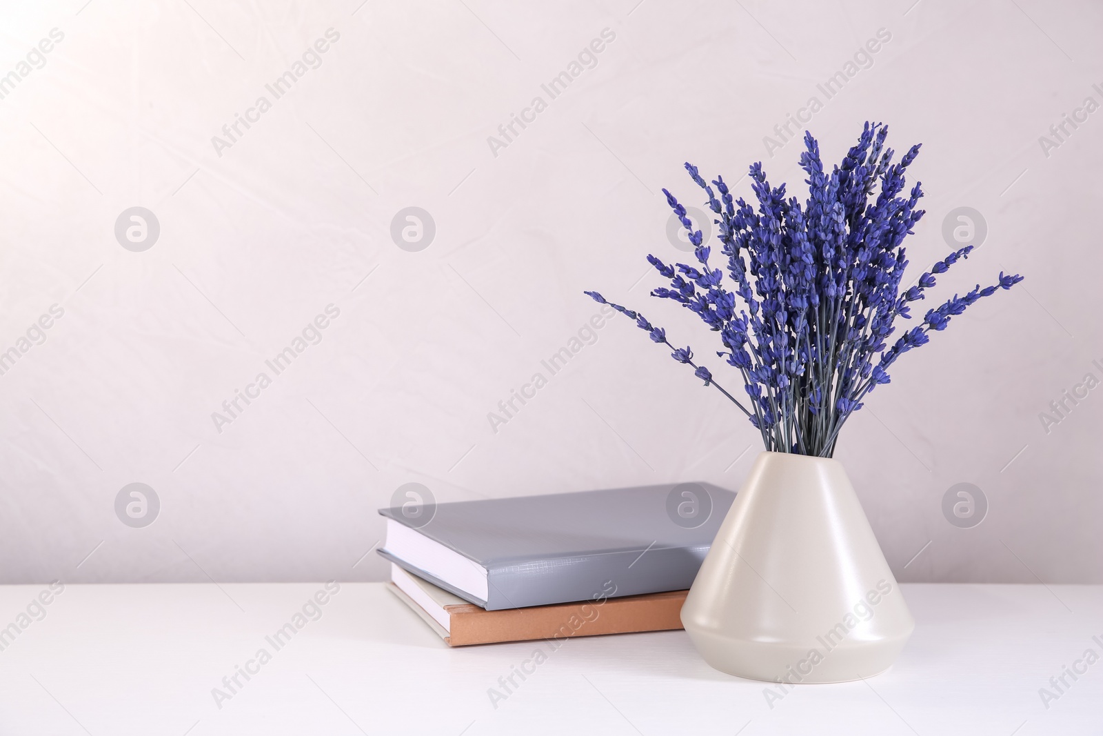 Photo of Bouquet of beautiful preserved lavender flowers and notebooks on white table near beige wall, space for text