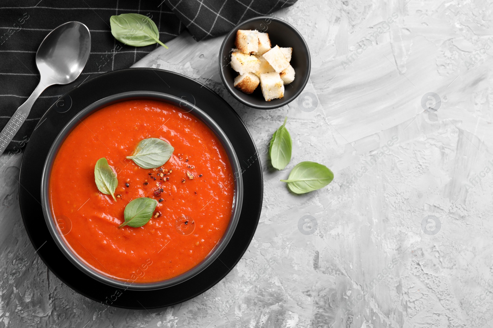 Photo of Delicious tomato cream soup served on grey textured table, flat lay. Space for text