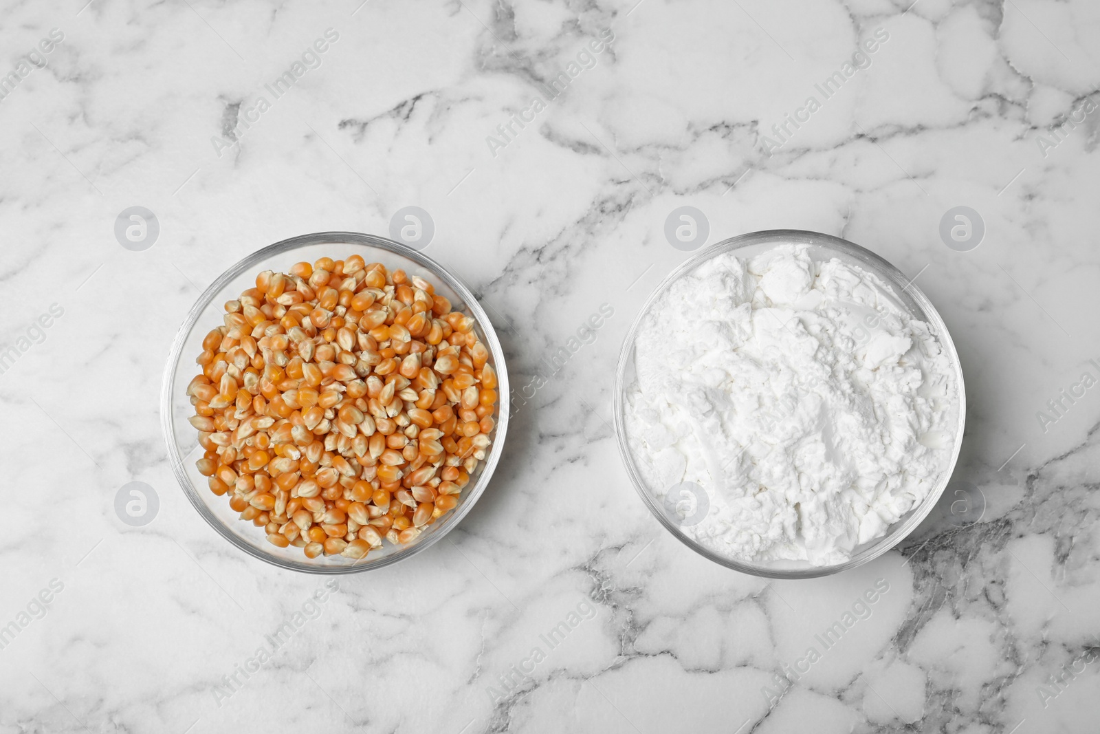 Photo of Bowls with starch and corn kernels on marble background, top view