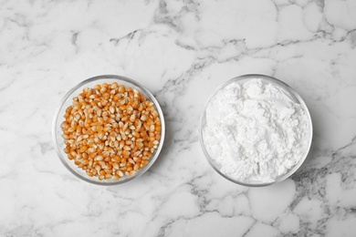 Photo of Bowls with starch and corn kernels on marble background, top view