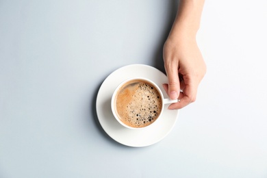 Photo of Young woman with cup of delicious hot coffee on light background, top view