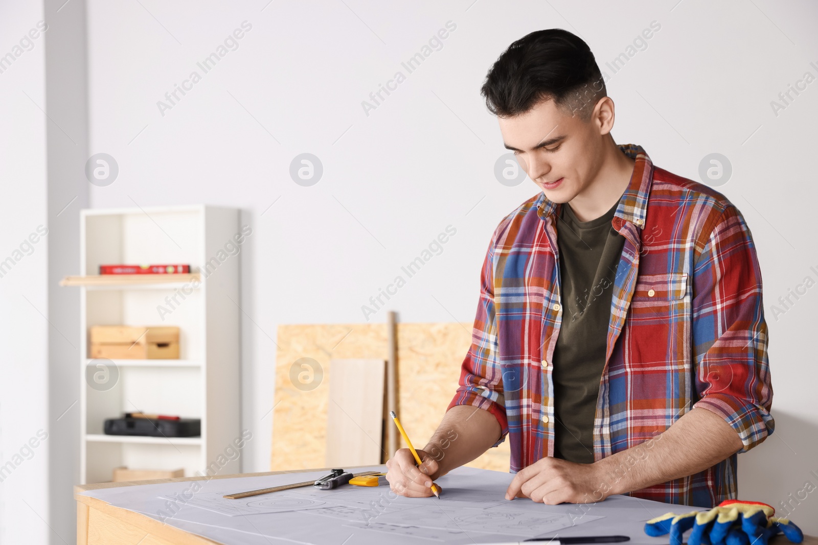 Photo of Young handyman working with blueprints at table in room