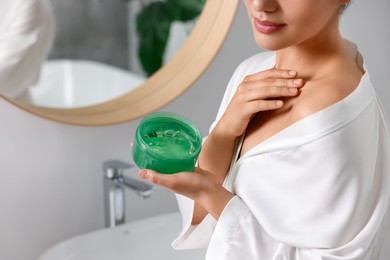 Photo of Young woman applying aloe gel onto her shoulder near mirror in bathroom, closeup. Space for text