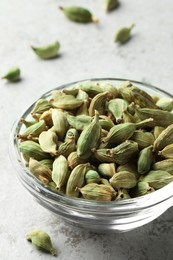 Photo of Glass bowl of dry cardamom pods on light grey table, closeup