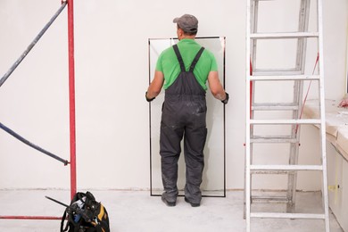 Worker holding double glazing indoors, back view. Window installation