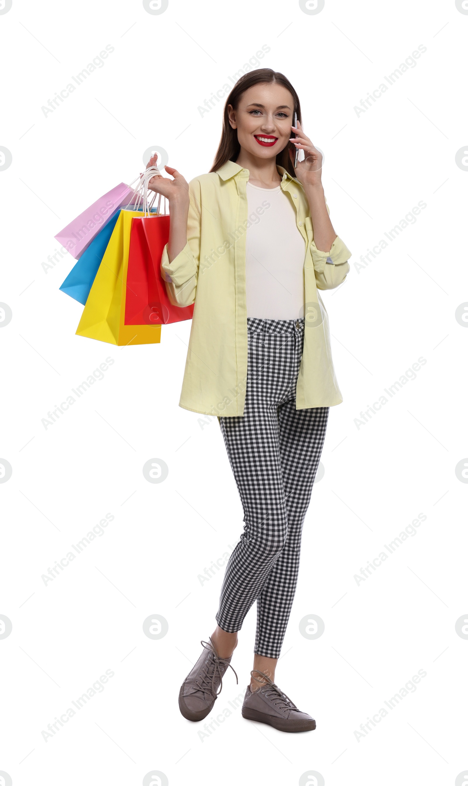 Photo of Stylish young woman with shopping bags talking on smartphone against white background