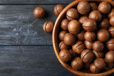 Photo of Bowl with organic Macadamia nuts and space for text on blue wooden background, top view