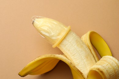 Photo of Banana with condom on pale orange background, closeup. Safe sex concept