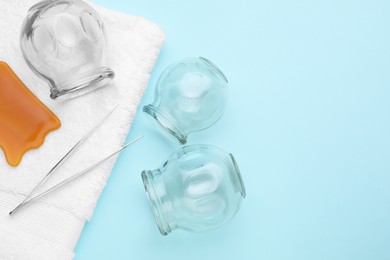 Photo of Glass cups, towel, tweezers and gua sha on light blue background, flat lay with space for text. Cupping therapy