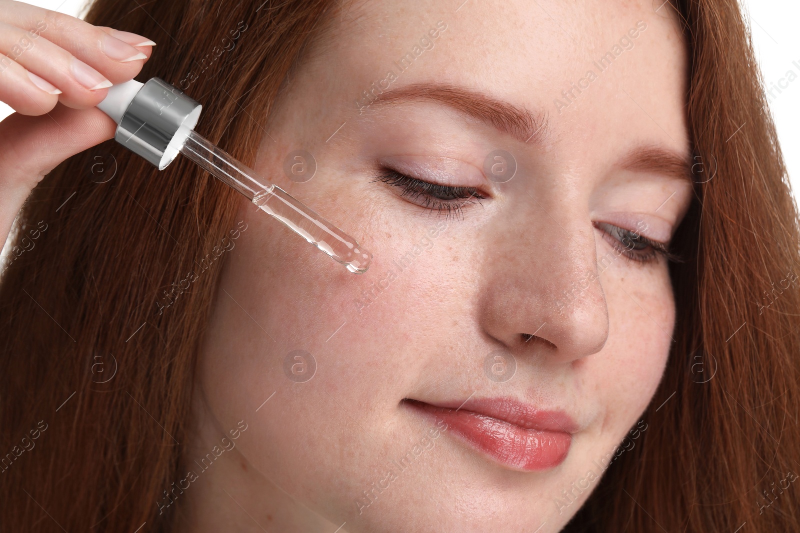 Photo of Beautiful woman with freckles applying cosmetic serum onto her face, closeup