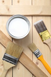 Photo of Can of white paint and brushes on wooden table, flat lay