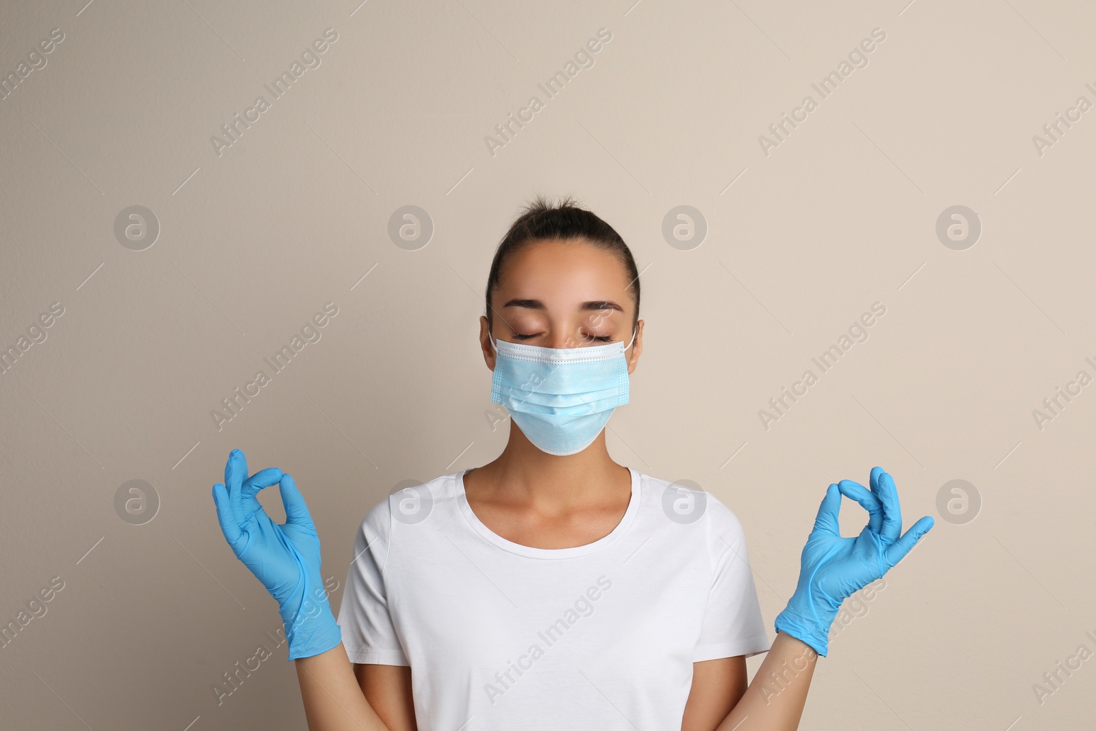 Photo of Woman in protective mask meditating on beige background. Dealing with stress caused by COVID‑19 pandemic
