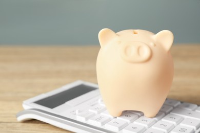Photo of Ceramic piggy bank and calculator on wooden table, closeup
