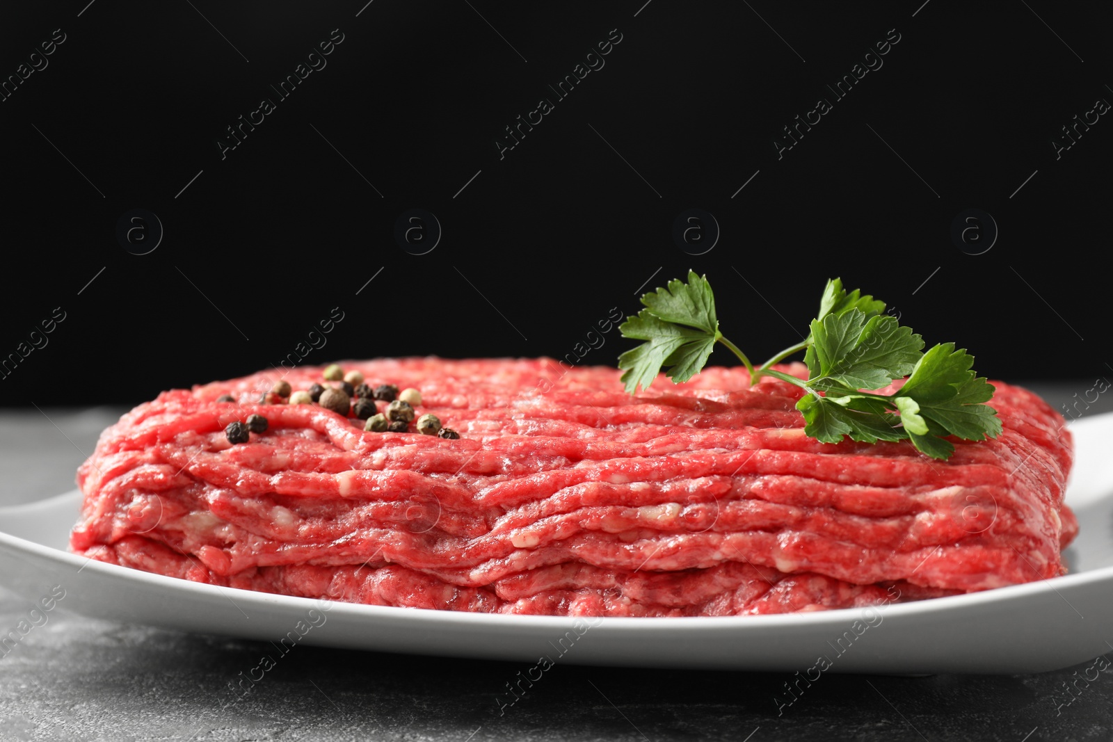 Photo of Raw ground meat, parsley and peppercorns on grey table, closeup