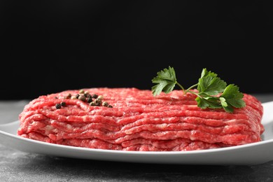 Raw ground meat, parsley and peppercorns on grey table, closeup