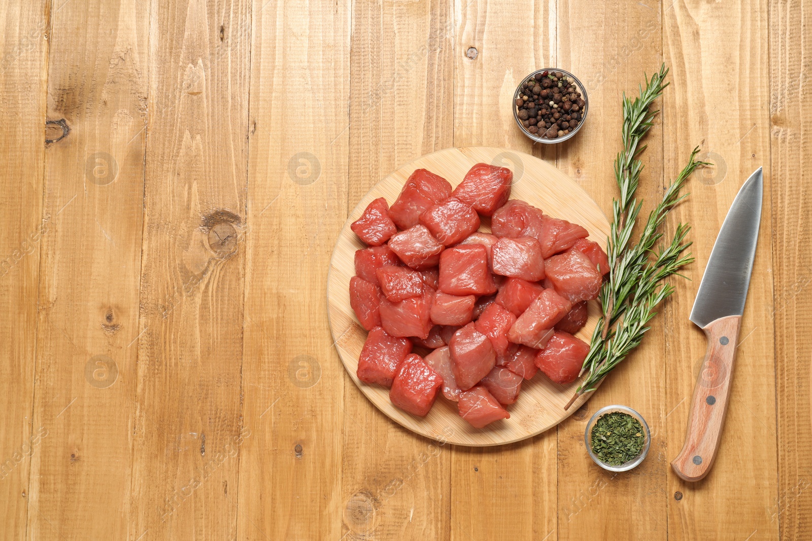 Photo of Cooking delicious goulash. Raw beef meat, knife and different spices on wooden table, flat lay. Space for text