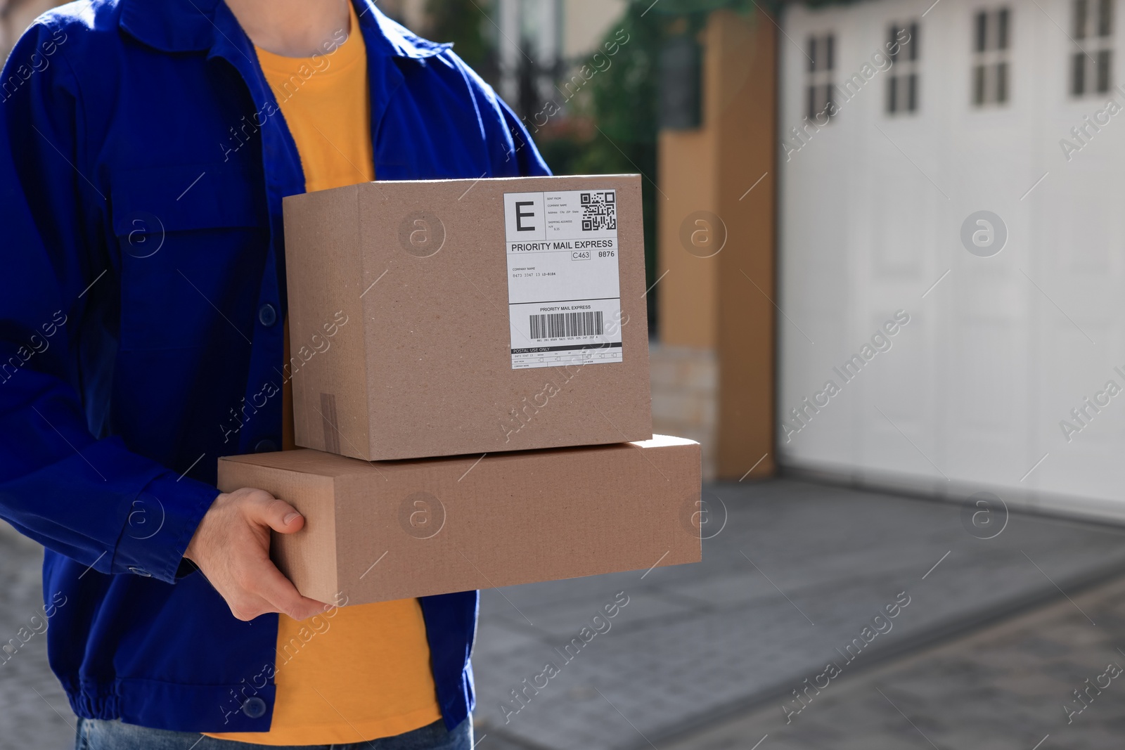 Photo of Courier carrying cardboard boxes near house outdoors, closeup