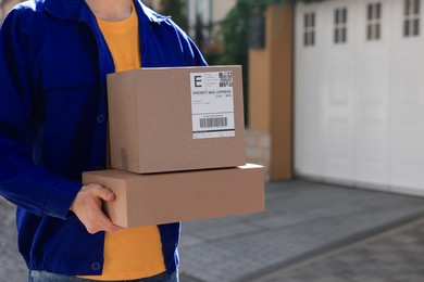 Courier carrying cardboard boxes near house outdoors, closeup