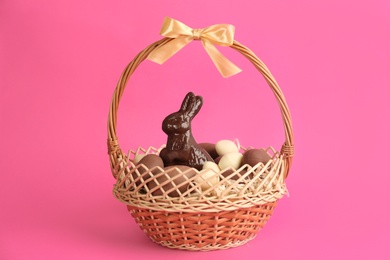Photo of Chocolate Easter bunny and eggs in basket on pink background
