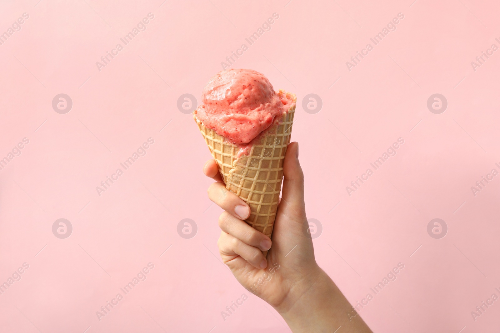 Photo of Woman holding waffle cone with delicious ice cream on pink background, closeup