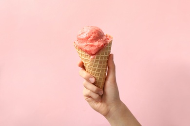 Woman holding waffle cone with delicious ice cream on pink background, closeup