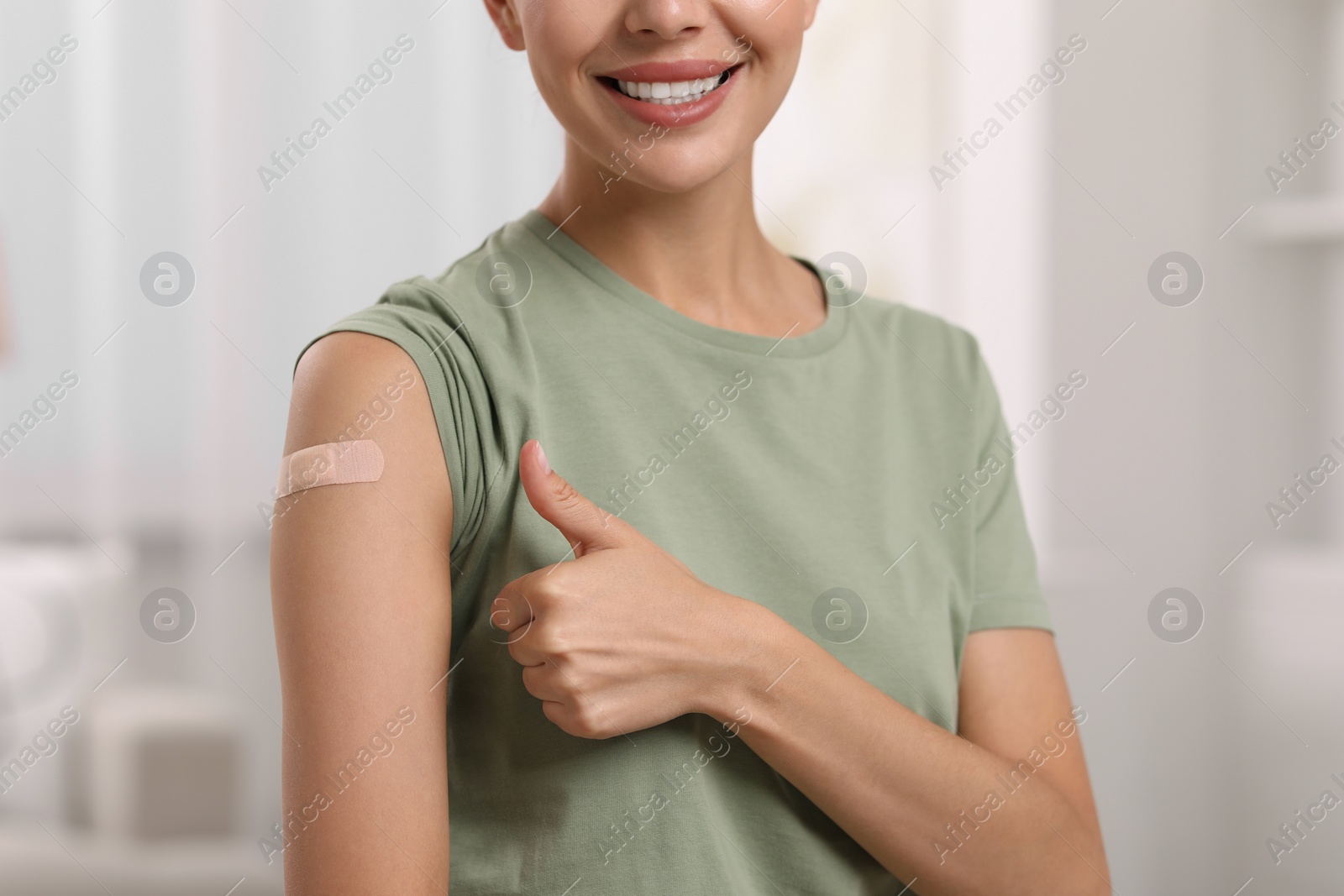 Photo of Woman with sticking plaster on arm after vaccination showing thumbs up at home, closeup