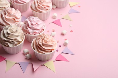 Photo of Delicious birthday cupcakes, bunting flags, marshmallows and sprinkles on pink background. Space for text