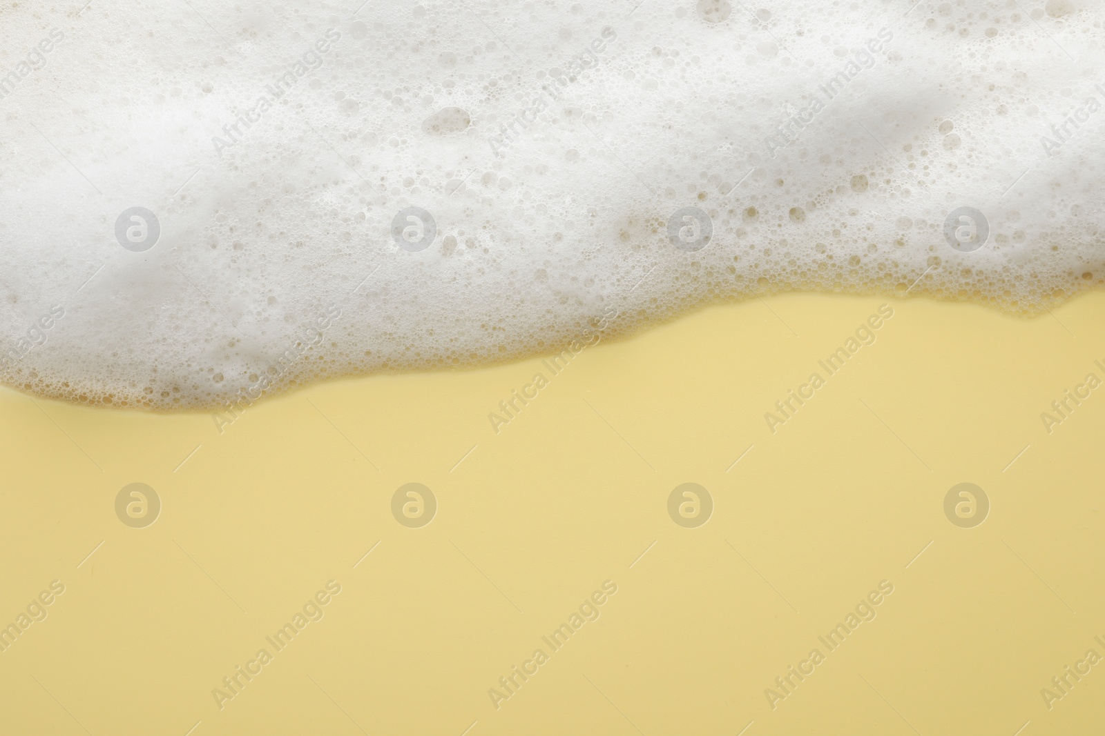 Photo of Fluffy soap foam on yellow background, top view. Space for text