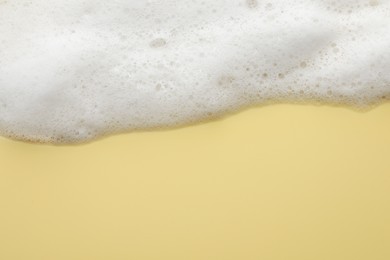 Photo of Fluffy soap foam on yellow background, top view. Space for text