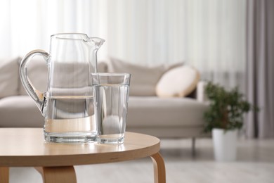 Photo of Jug and glass with clear water on wooden table indoors. Space for text