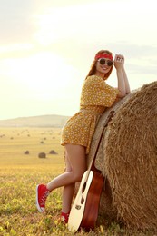Happy hippie woman with guitar near hay bale in field