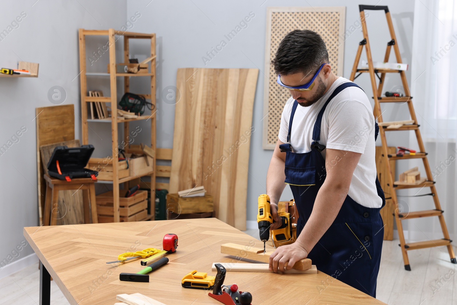 Photo of Young worker using electric drill at table in workshop