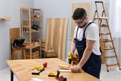 Young worker using electric drill at table in workshop