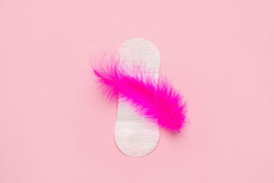 Photo of Sanitary pad with feather on pink background, top view. Menstrual cycle