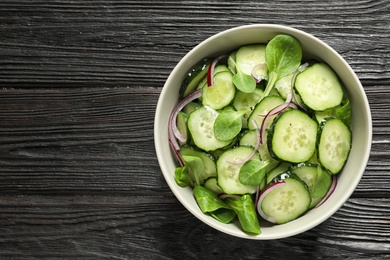 Photo of Delicious cucumber salad with onion and spinach in bowl on wooden background, top view. Space for text