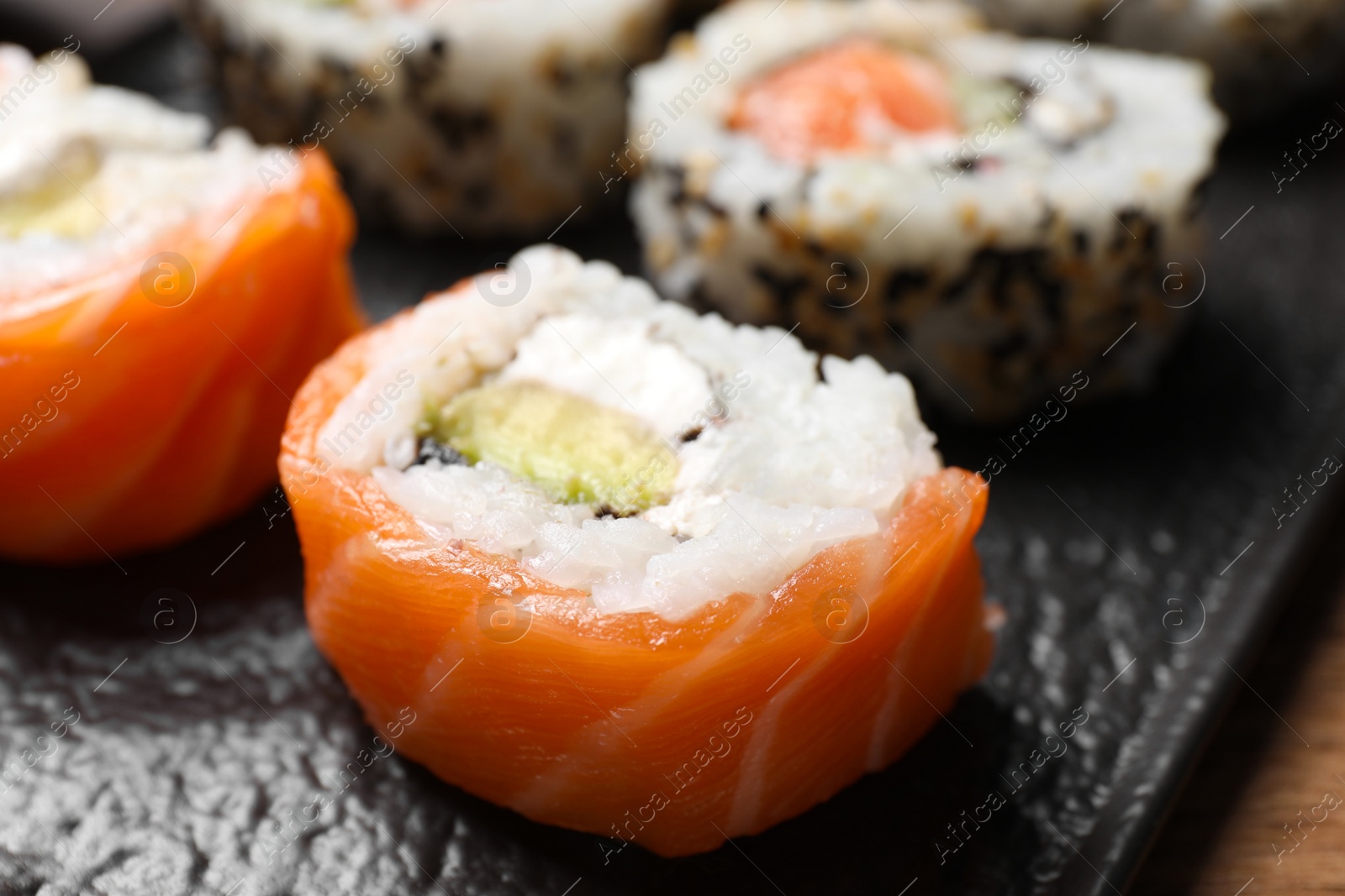 Photo of Delicious sushi rolls on black plate, closeup