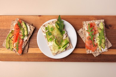 Photo of Fresh crunchy crispbreads with cream cheese, cucumber, green onion, salmon and arugula on beige table, top view