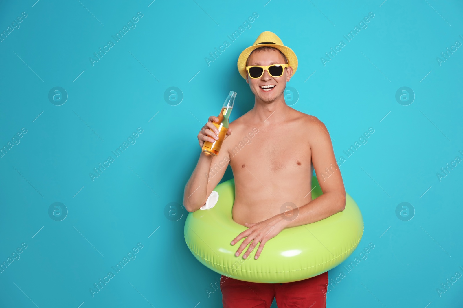 Photo of Shirtless man with inflatable ring and bottle of drink on color background