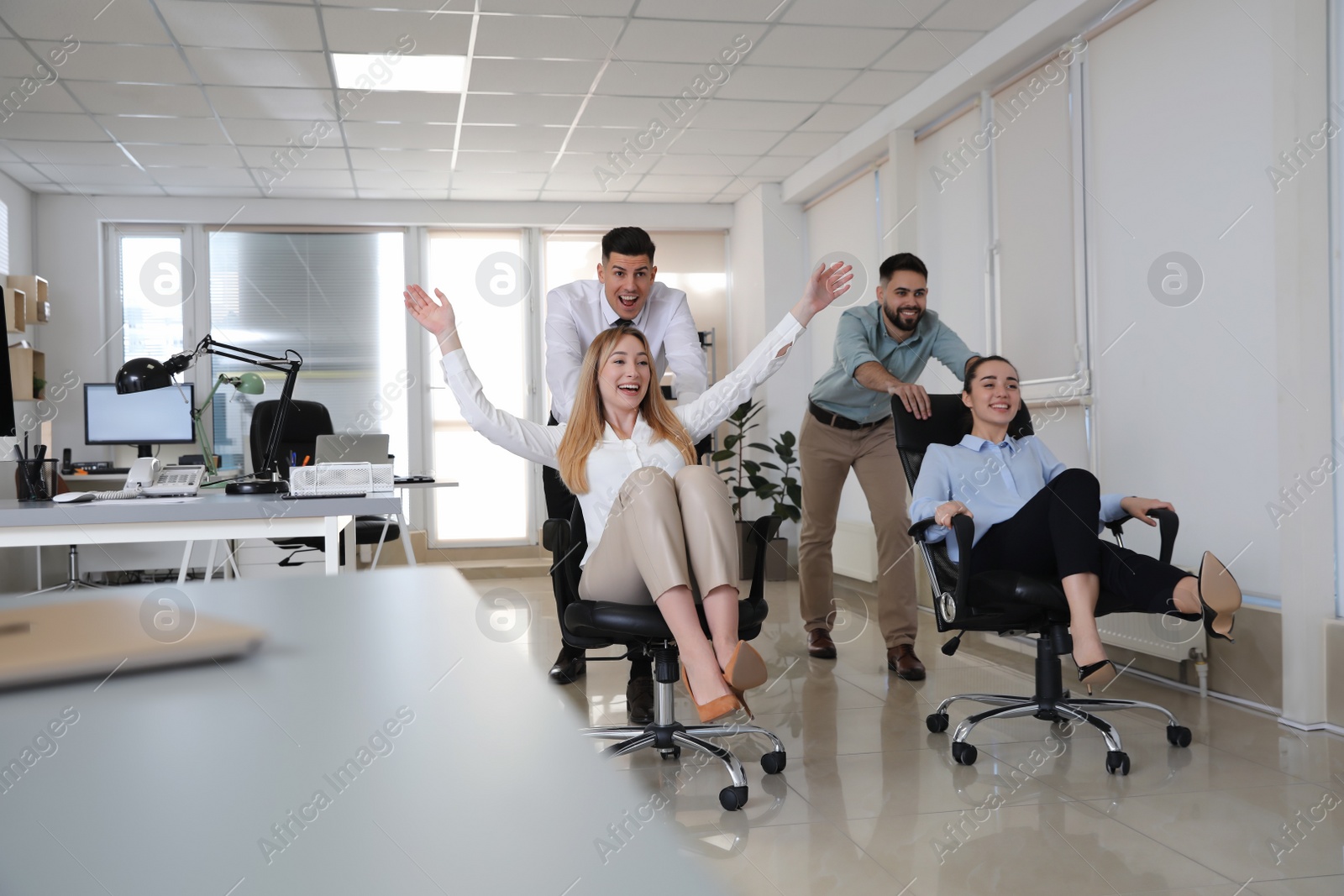 Photo of Happy office employees riding chairs at workplace