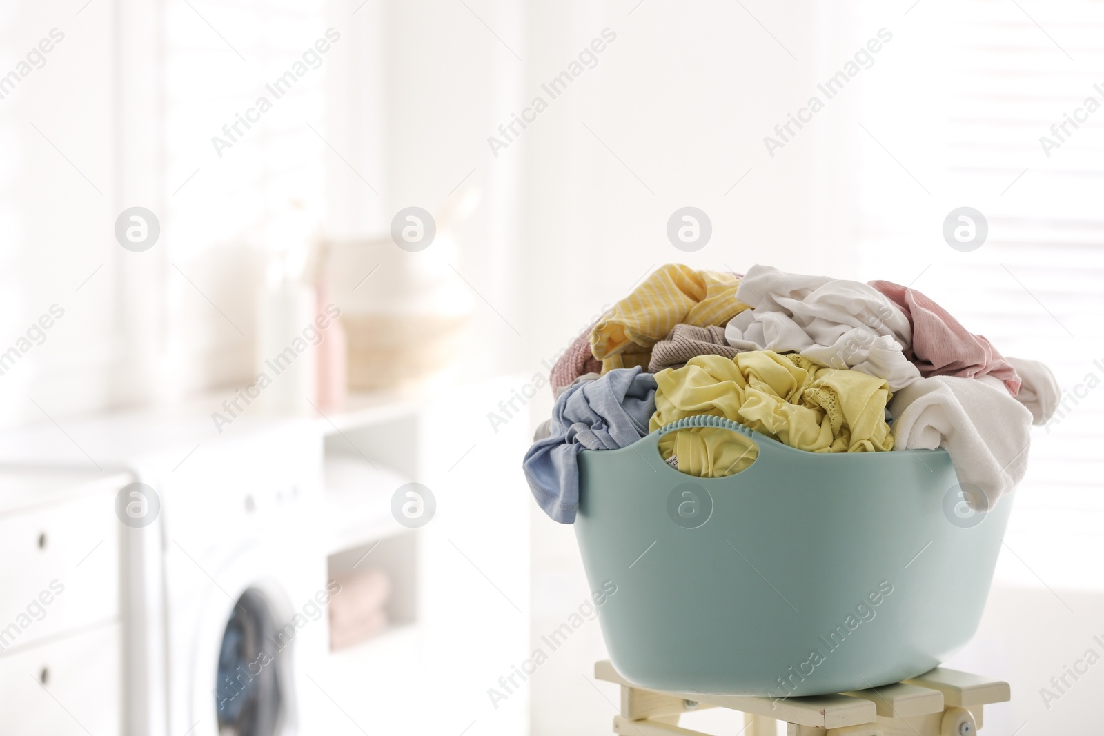 Photo of Light blue basket with dirty laundry on wooden stand indoors, space for text
