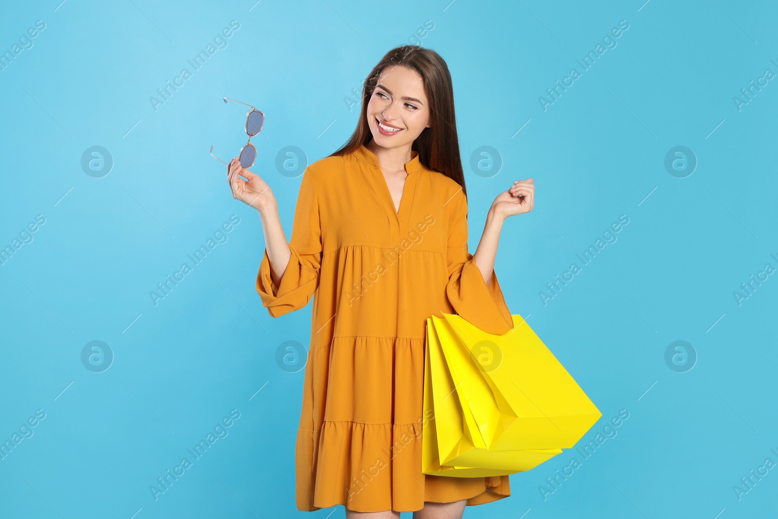 Photo of Happy young woman with shopping bags on light blue background. Big sale