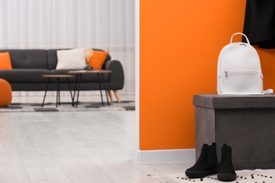 Photo of Pouf with backpack and shoes near orange wall in stylish room, space for text. Interior design