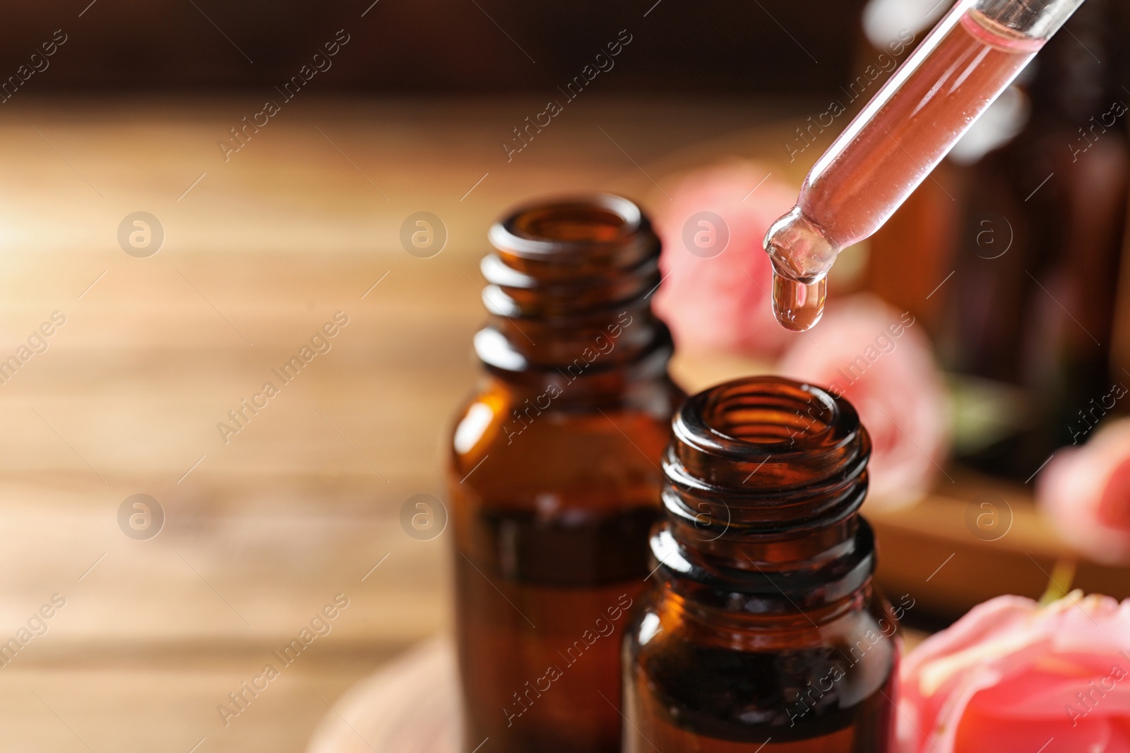 Photo of Dripping rose essential oil into bottle against blurred background, space for text