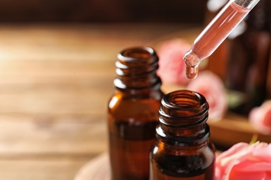 Photo of Dripping rose essential oil into bottle against blurred background, space for text