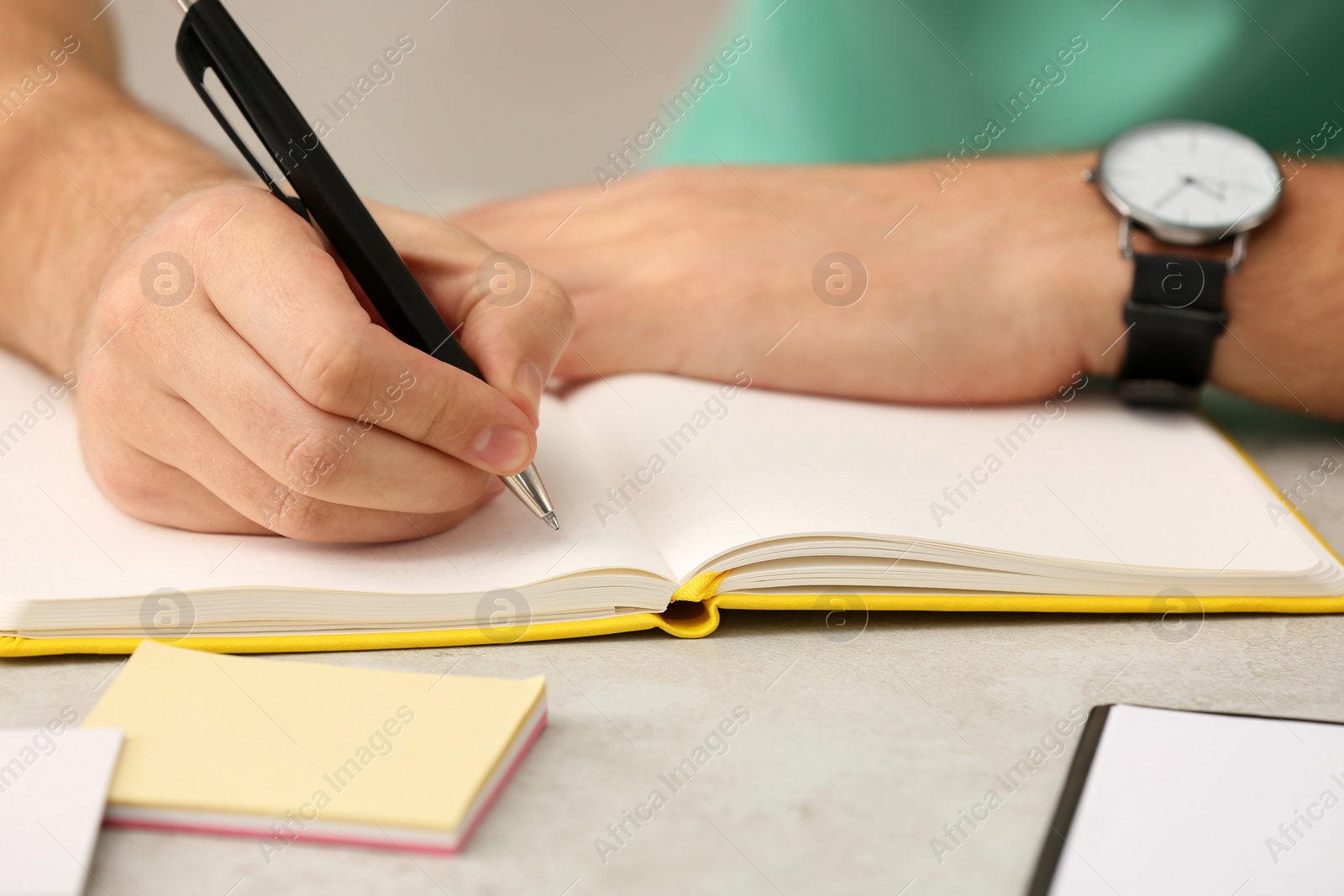 Photo of Man writing in notebook at table indoors, closeup