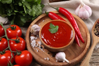 Photo of Delicious ketchup in bowl, products and spices on wooden table, closeup. Tomato sauce